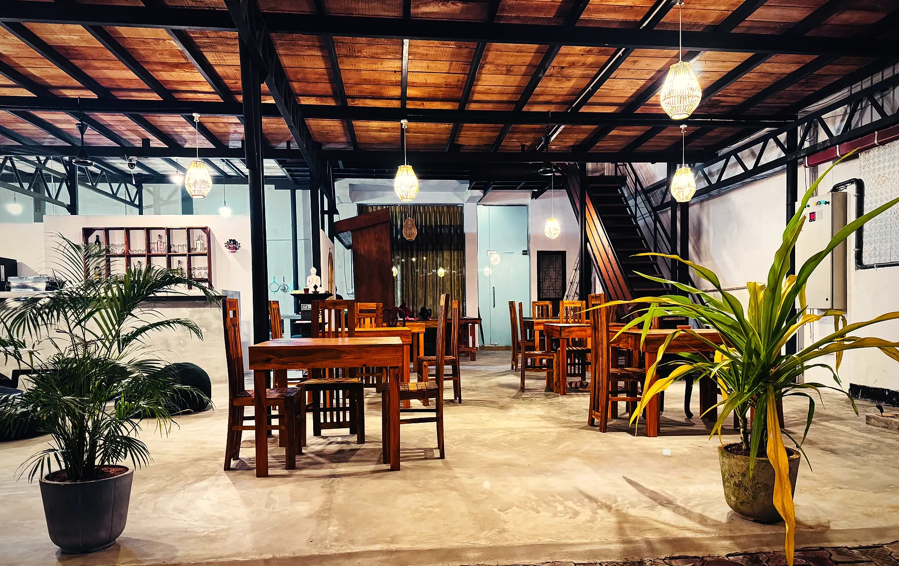 Teak tables and potted palms beneath Meyola's timber roof and woven lanterns